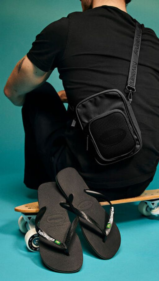 Chanclas Havaianas negras unisex junto a un monopatín y bolso negro, sandalias Havaianas originales para hombre y mujer, calzado cómodo y casual para verano